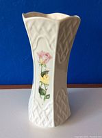 Front angled view of white ceramic embossed vase with floral design against blue background.