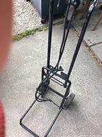 Front angled view showing black metal frame, folding handle, two wheels, and straps.