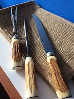 Three piece cutlery set including fork, knife, and sharpener with carved wood or antler style handles on burlap background
