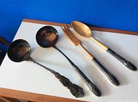 Four vintage serving utensils including a Gorham ladle on left, and three other utensils with partially wooden handles showing patina.