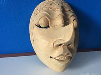 Front angle view of a vintage, light-colored wooden mask showing closed eyes, ornate forehead, and smiling mouth with detailed teeth carving.