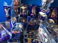 Eighteen Bratz dolls in original sealed plastic bags, assorted characters, arranged on a surface against a blue wall.