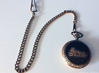 Copper pocket watch with chain; focus on embossed train design on cover.