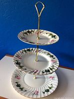 Three-tier plate stand assembled with floral decorated porcelain plates and brass central rod with handle.