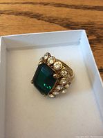 KJL emerald green and rhinestone ring in a white box on wood surface.