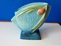 Front view of the Roseville pottery vase with blue-green glaze and pinecone decoration.