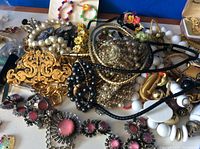 Wide shot of assorted scrap jewelry including various beads, necklaces, floral accessories, and a large decorative gold-toned pendant piece