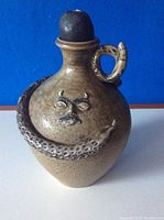 Front view of vintage stoneware snake jug with lidded top and face detail.