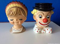 Front view of vintage boy and clown ceramic head vases on blue background.
