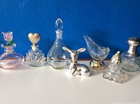 Seven vintage perfume bottles displayed on blue background, showing variety in glass and silver-tone decorative elements.