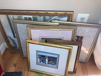 Five framed prints leaning against a wall, showing variation in frame styles and sizes
