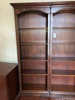 Full front view of wooden bookshelf showing four shelves, arched top, and decorative carved sides
