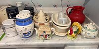 Full assortment of ceramic and metal kitchen canisters, teapots, jugs, tureens, gravy boat, ladle and decorative containers on marble countertop, showing variety and condition.