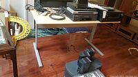 Computer table viewed from front left angle with electronic devices and cables on top.