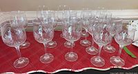 Full set of 16 crystal wine glasses arranged on a red cloth with a subtle plaid pattern, showing all glasses upright with clear stems and patterned bowls.