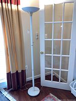 Full view of the white floor lamp with gold accents beside a door and curtain.