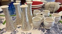 Photo of five white porcelain Lenox candle holders with gray floral designs placed side by side on a floral patterned cloth.
