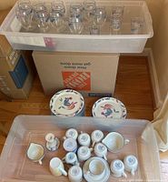 Plastic bins with dinnerware plates stacked and the coffee cups, saucers, and milk jugs placed upside down, showing 9 plates, 8 cups, 2 saucers, and 2 milk jugs.