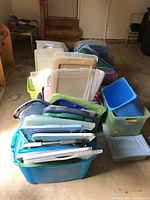 Various plastic storage bins and their lids stacked in a pile inside a garage or storage room.