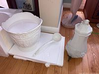 Wide shot of white ceramic punch bowl with ladle and ceramic tea server on a shelf.