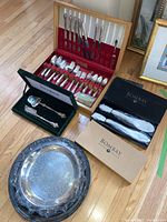 Full view of all items including flatware set in wooden case, serving utensils in green velvet box, Bombay platters in boxes, wooden cutting board on floor