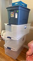 Stack of four plastic storage containers including one large blue solid bin and three clear Sterilite bins with lids.