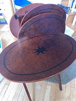 Set of four oval wooden TV trays stacked with the top tray showing the compass star design and black oval border on a brown wood grain finish.