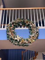 Full view of the large decorative wreath showcasing its circular shape and assorted winter-themed decorations against a railing background.