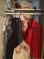 Closet view showing men's slacks and western shirts hanging on rod, tote bags and umbrellas folded and stacked on shelves above.