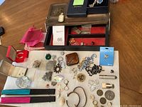 Wooden jewelry box holding various pieces of jewelry and small accessories laid out on a paper towel with colorful folding fans placed below