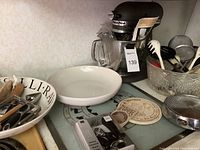 KitchenAid mixer with bowl and various ceramic serving dishes, utensils in bowl, hand exercisers, vintage warming trivet