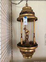Gold-tone metal rain lamp with chain, glass rods, and nude female figure inside cylindrical enclosure