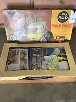 Original box opened showing plastic sprues, chrome parts and decal sheet visible through top panel cutout; box art depicts yellow Show-Go Roadster.