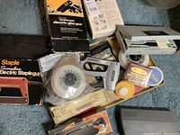 View of entire lot showing Swingline electric stapler box, Thermogrip glue gun box, flexible screwdriver, small toolset, white sticky tape rolls, and Sergio flex bandage kit.