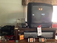 Photo showing small CRT television on wooden stand with DVD VHS player, remotes, Kodak film container, and Buccaneers keychain bags.