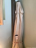 Photo showing the beige canvas outdoor umbrella closed and standing upright with a visible brand strap labeled 'ButterFly'. The projector screen is not fully visible in this image.