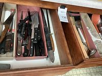 Drawer with multiple knives including chef knives, serrated knives, and others with plastic and wooden handles.