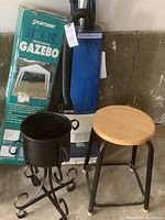 Photo showing Panther Matic upright vacuum cleaner, boxed Sportsman gazebo, black metal planter pot on wrought iron stand, and wooden stool with metal legs.