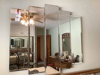 Photo of a wall-mounted mirror composed of five vertical mirrored panels reflecting a room with furniture and a ceiling fan.