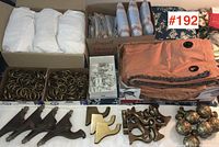 Three sets of folded curtains including white and patterned fabrics, boxes of brass-tone curtain rings, curtain hooks, and orange patterned curtain panels