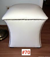 Front view of square white faux leather ottoman with visible silver nailhead trim.