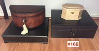 Wide photo showing three storage boxes on floor: large brown semi-circular jewellery box, black rectangular box, and small hexagonal wooden box
