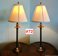 Pair of table lamps shown lit side by side on a round wooden table against light blue wall.