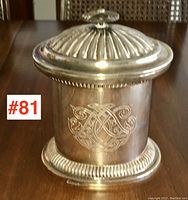 Front view of silver plated tea caddy showing engraved monogram and ribbed details on lid and base.