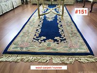 Full length view of blue and beige wool runner with floral border and cream fringe, showing length and placement on wood floor