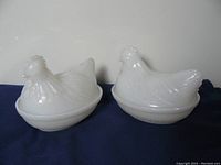 Two milk glass hen on nest covered dishes shown side-by-side on dark cloth background. Hen lids placed on the matching dish bases.