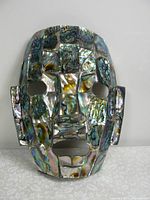 Front view showing the full face mask with iridescent abalone shell pieces forming the contours and features.