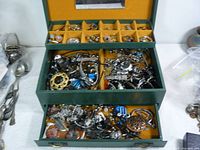 Top compartment of jewelry box showing assorted rings and brooches in individual slots lined with yellow velvet.