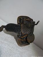 Side angle photo of a brown leather Western horse saddle with metal studs and detailed tooling, showing wear and use.