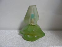 Side view showing green glass lip-shaped bottle with frosted cap resembling an abstract figurative shape.